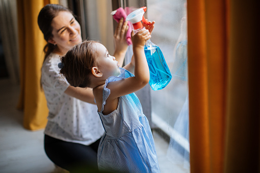 Cropped shot of a mother and her little daughter cleaning a living rooms window together at home