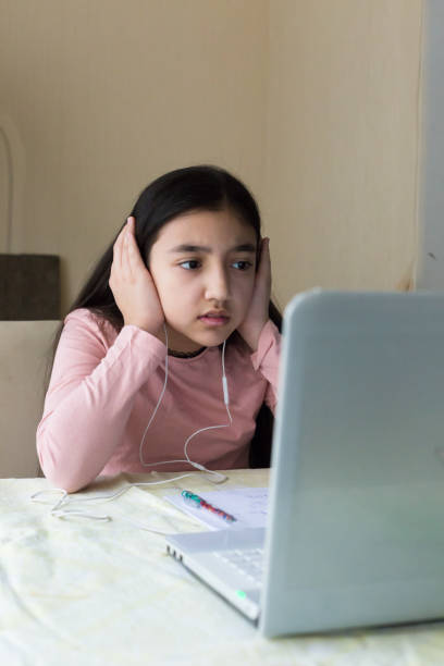 istock Young girl thinking over a problem at the table with laptop at home schooling, online virtual classroom video conference, distant education. Internet network connection problem, unhappy child. 1251591578