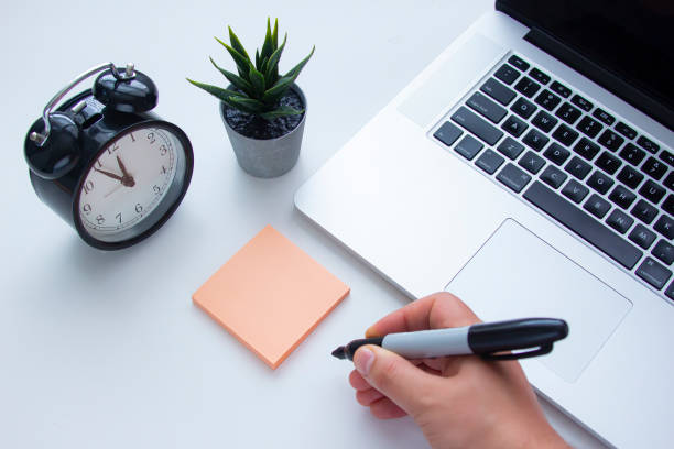 istock A person about to write a note next to a laptop keyboard with a clock and a plant on a white table 1251601402