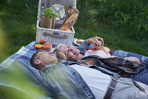 Happy mature couple is lying on grass ang embracing after eating healthy meals in green wood