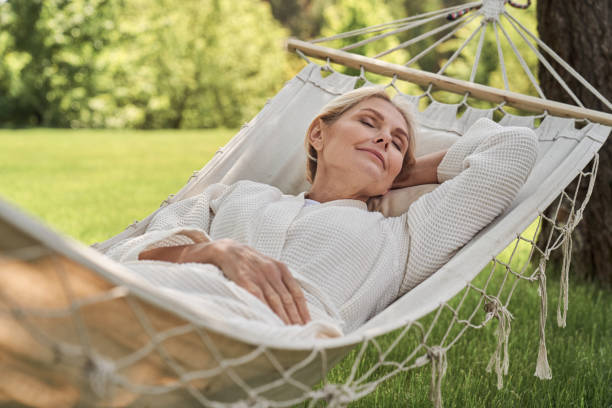 Happy mature female sleeping in hammock outdoors Smiling beautiful woman is having rest in green yard in open air on sunny warm day wife stock pictures, royalty-free photos & images