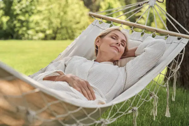 Photo of Happy mature female sleeping in hammock outdoors