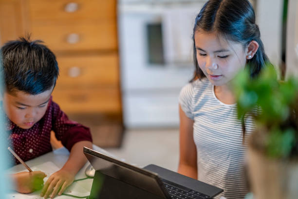 istock 11 year old girl doing an online class while sitting at kitchen table with her brother 1251608993