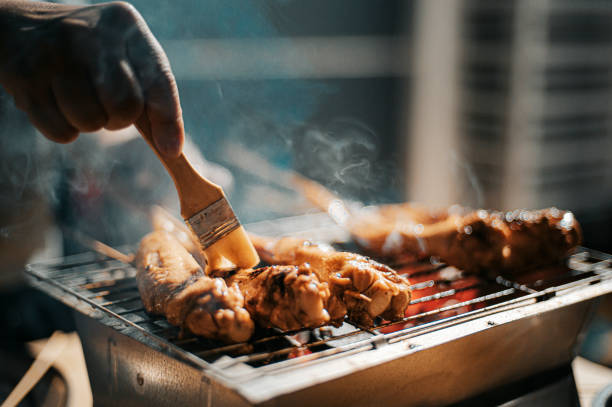 a night bbq party gathering with food preparation brushing and applying oil and honey on chicken wing a night bbq party gathering with food preparation marinated photos stock pictures, royalty-free photos & images