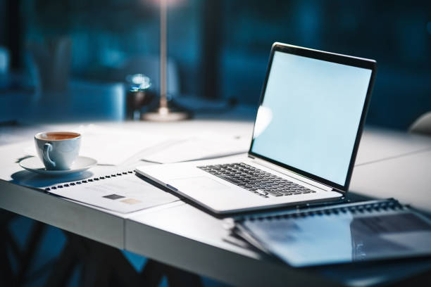The perfect setting to complete work Shot of a laptop on a desk in a modern office at night with no people office desk stock pictures, royalty-free photos & images
