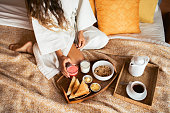 Healthy breakfast in bed with granola, crispy toast, butter, milk and jam. Woman hand holding watermelon juice on wooden tray.