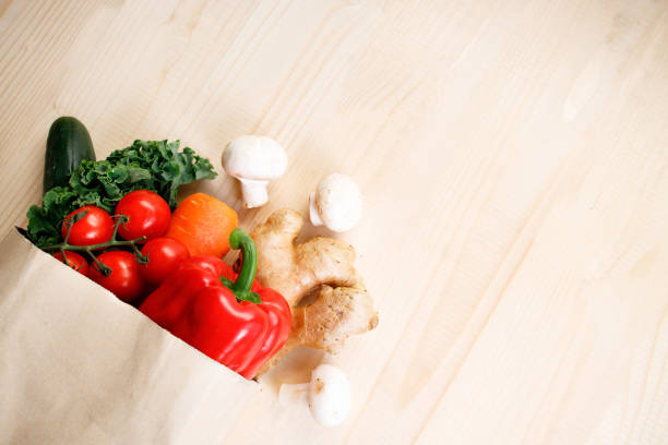 Fresh vegetables in paper bag on light wooden background. Food bag and eco-friendly concept. Healthy food background.
