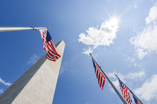 National flag of The United States of America with bright sunny shine in the background. Location - Washington DC - The George Washington Monument