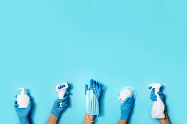 levantadas las manos en guantes médicos sosteniendo máscaras, desinfectantes, jabón, termómetro sin contacto sobre fondo azul. bandera. copiar espacio. equipo de protección de la salud durante la cuarentena pandemia de coronavirus - communicable disease fotografías e imágenes de stock