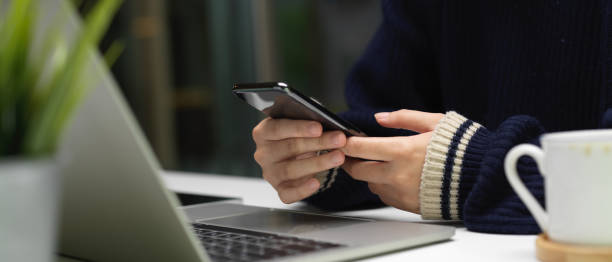 istock Female worker using smartphone while working with laptop on simple office desk 1251656652