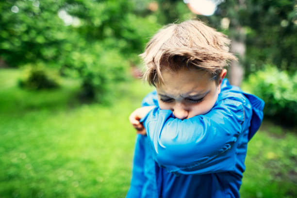 Sick little boy is coughing into elbow in his backyard\nNikon D850