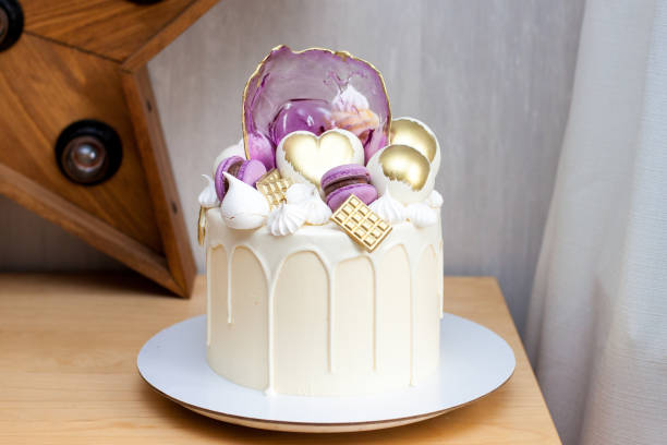 Modern elegant cake with melted white chocolate, golden heart and chocolate balls, macaroons, meringue and caramel. Modern elegant birthday cake with melted white chocolate, golden heart and chocolate balls, macaroons, meringue and caramel. purple velvet cakes stock pictures, royalty-free photos & images