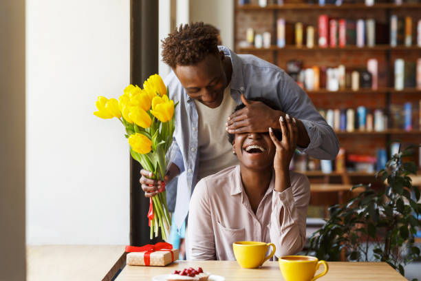 ragazzo afroamericano che regala fiori alla sua ragazza nel caffè urbano - men african descent giving flower foto e immagini stock