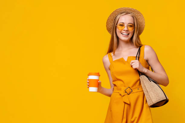 Positive Teen Girl Holding Cup With Takeaway Drink And Smiling At Camera Positive Teen Girl Holding Cup With Takeaway Drink And Smiling At Camera While Posing On Yellow Background WIth Copy Space jumpsuit stock pictures, royalty-free photos & images