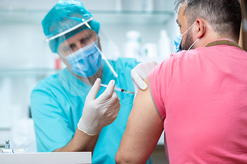 Doctor wearing protective workwear injecting vaccine into patient's arm