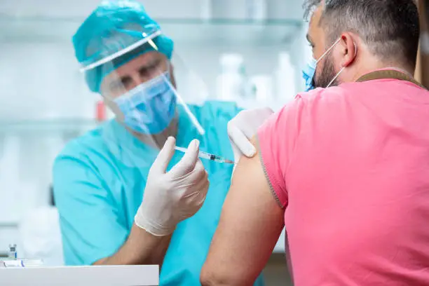 Photo of Doctor wearing protective workwear injecting vaccine into patient's arm