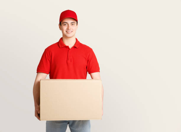 istock Work of modern postman. Smiling young guy in uniform holding big cardboard box 1251666446