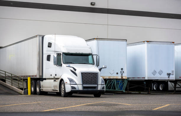 istock Big rig white semi truck with dry van semi trailer loading cargo in warehouse dock beside another semi trailers 1251666712
