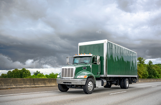 Pequeño y potente camión semi de plataforma verde con remolque de caja que corre en la carretera con cielo tormentoso en el fondo photo