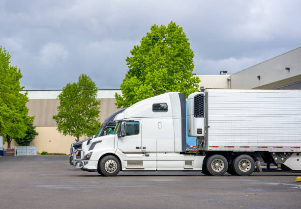 istock Big rig semi trucks with refrigerator semi trailer loading frozen cargo standing at warehouse dock gates 1251666775
