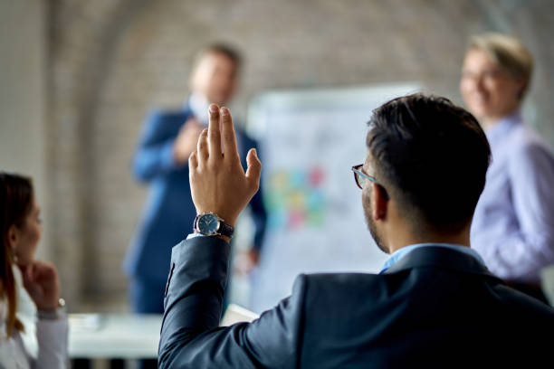 I have a question! Rear view of a businessman raising his hand to ask the question during business presentation in the office. hand raised photos stock pictures, royalty-free photos & images