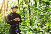 Young rider standing in forest, holding mobile phone
