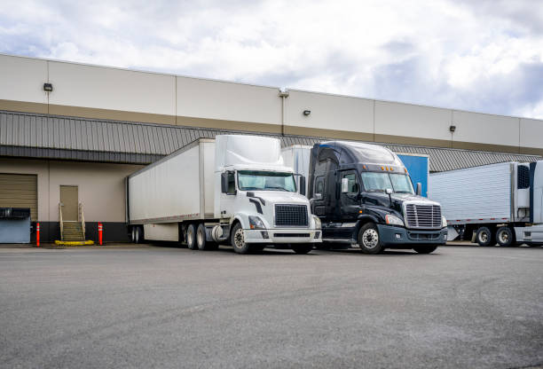 istock Black and white big rigs semi trucks with semi trailers loading cargo at warehouse dock with gates for each 1251670131