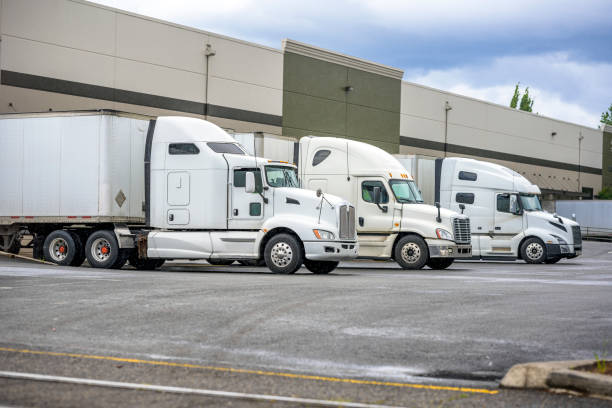 istock Different models of big rigs semi trucks with dry van semi trailers loading cargo at warehouse docks with rain weather 1251671538