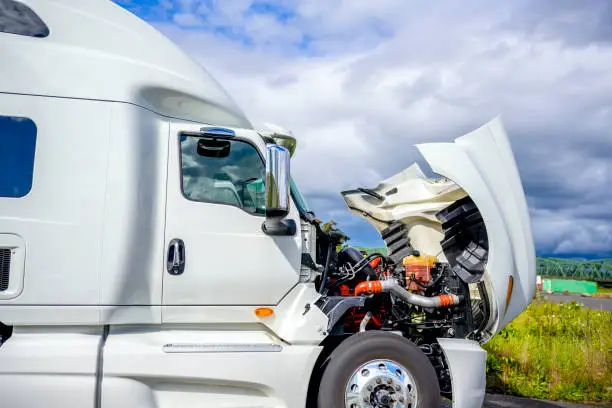 Photo of Broken white big rig semi truck tractor stands on the side of the road with an open hood awaiting mobile repair assistance