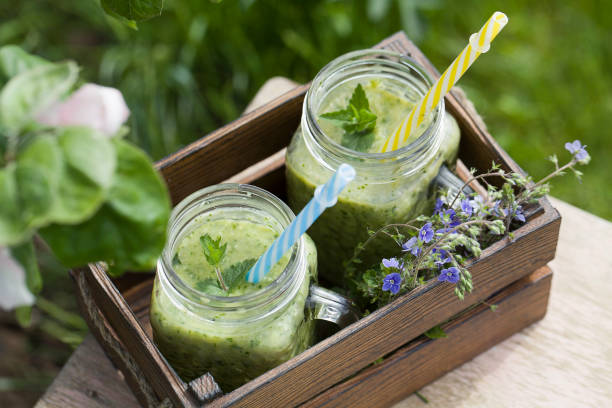 grüner smoothie auf altem hocker in der nähe von blumen auf der natur - chlorophyll green smoothie smoothie vegetable stock-fotos und bilder