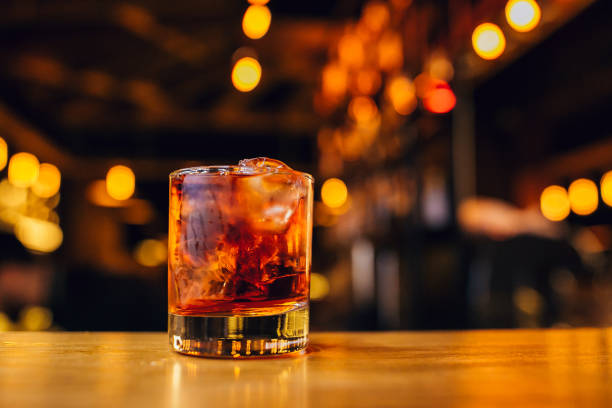 bicchiere con whisky e cubetti di ghiaccio sul bar con bokeh sullo sfondo. - whisky cocktail glass rum foto e immagini stock