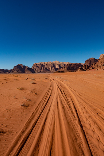 Car tire tracks on the orange desert sand among the rocks in the Wadi Rum desert in the Jordanian part of the Arabian desert.