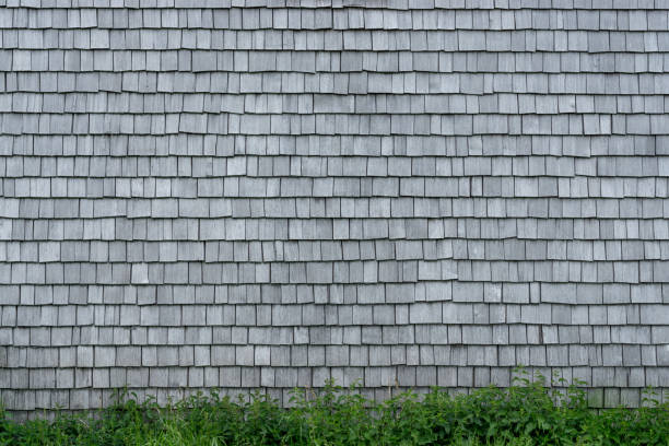 Old weathered Shingles wooden wall background. Traditional shakes with nice grey texture and Grass in Foreground. Bavaria, Allgau, Germany.