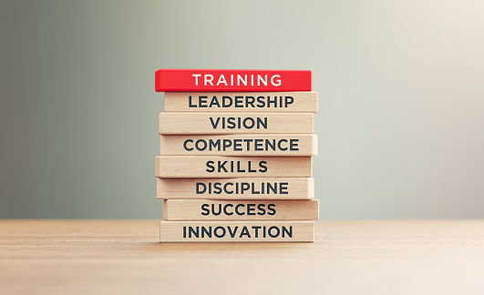 Training related words written woodblocks sitting on wood surface in front of a defocused background. Training concept.