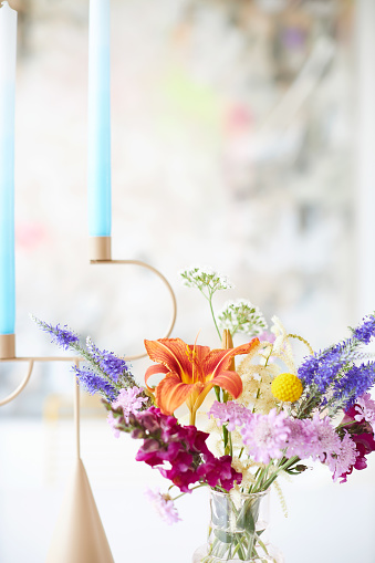 A wonderfully colorful bouquet of flowers on a white dining table, with flowers in the colors apricot, blue, red and pink