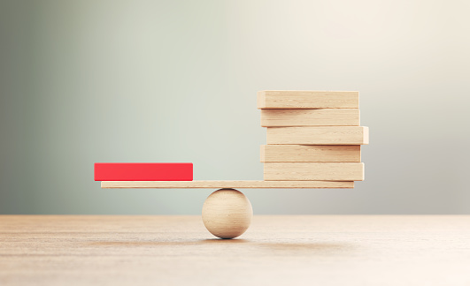Wooden seesaw scale and wooden blocks sitting on wood surface in front of defocused background. Balance concept.