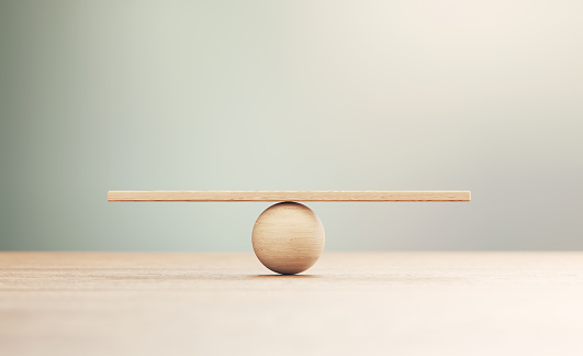 Wooden seesaw scale sitting on wood surface in front of defocused background. Balance concept.