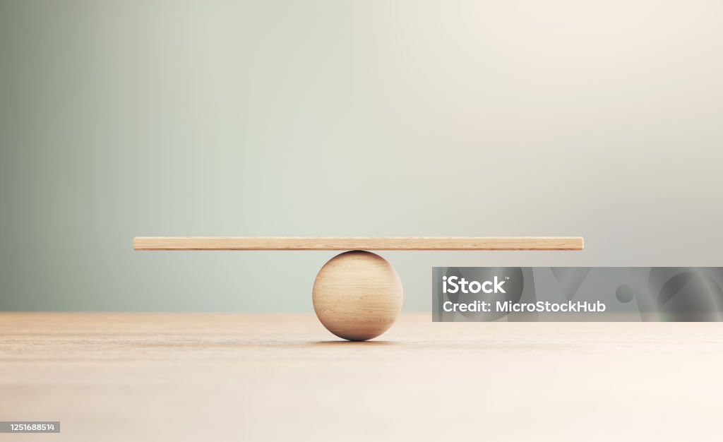 Wooden Seesaw Scale Sitting on Wood Surface in Front of Defocused Background Wooden seesaw scale sitting on wood surface in front of defocused background. Balance concept. Balance Stock Photo