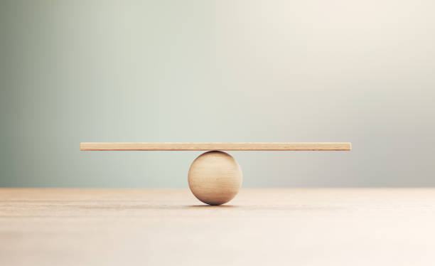 Wooden Seesaw Scale Sitting on Wood Surface in Front of Defocused Background Wooden seesaw scale sitting on wood surface in front of defocused background. Balance concept. scale stock pictures, royalty-free photos & images