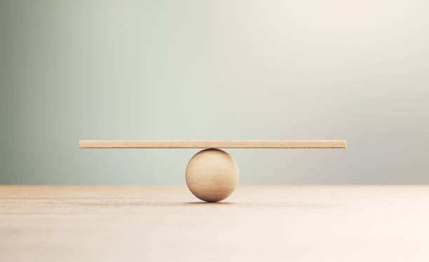 wooden seesaw scale sitting on wood surface in front of defocused background - balance imagens e fotografias de stock