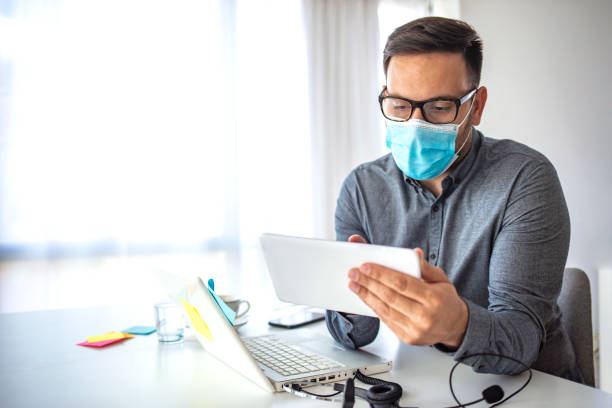 istock Businessman looking at a tablet PC wearing a healthcare face mask 1251688607