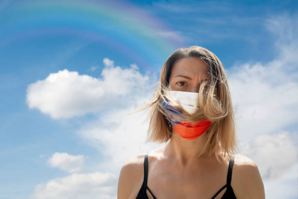 istock Woman is Looking into Camera While Wearing Czech Flag Protective Mask To Avoid Coronavirus Covid-19 Against Cloudscape with Rainbow 1251692314