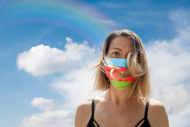 istock Woman is Looking into Camera While Wearing Azerbaijan Flag Protective Mask To Avoid Coronavirus Covid-19 Against Cloudscape with Rainbow 1251692850