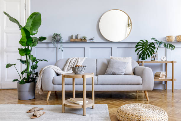 istock Stylish living room interior with design grey sofa, coffe table, rattan pouf, basket, shelf, mirror, tropical plants, decoration, carpet and elegant personal accessories in modern home decor. 1251692994