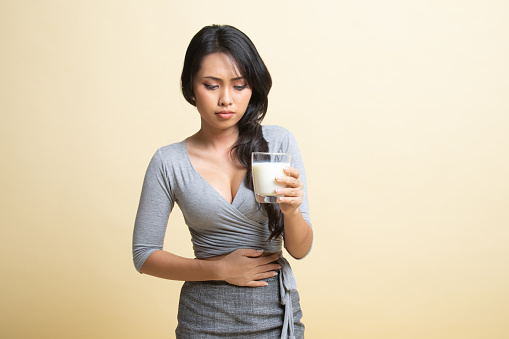 Asian woman drinking a glass of milk got stomachache   on beige background