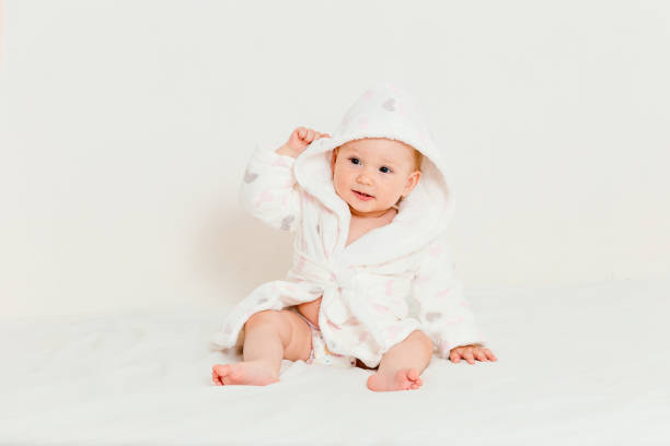 Baby in a bathrobe after bathing sits on a bed on a white background