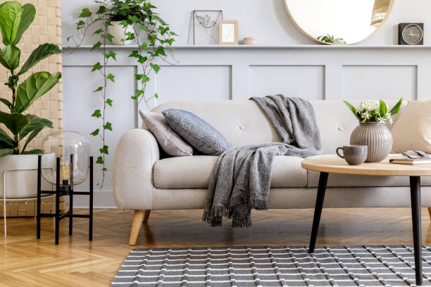 Photo of Scandinavian concept of living room interior with design sofa, coffee table, plant in pot, flowers, carpet, plaid, pillow, shelf, decoration and personal accessories in modern home staging.