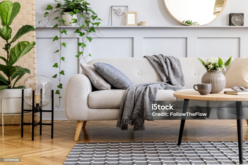 斯堪的納維亞概念的客廳室內設計沙發,咖啡桌,植物在鍋,鮮花,地毯,格子,枕頭,貨架,裝飾和個人配件在現代家庭舞臺。 - 免版稅住宅內部圖庫照片