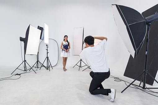 An Asian photographer is photographing a model posing in a white photography scene for advertising in a magazine.