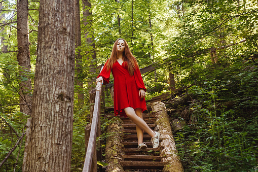 The young woman in red dress in old stairs in forest. Concept of nature and happy life, adventure. Beautiful light.